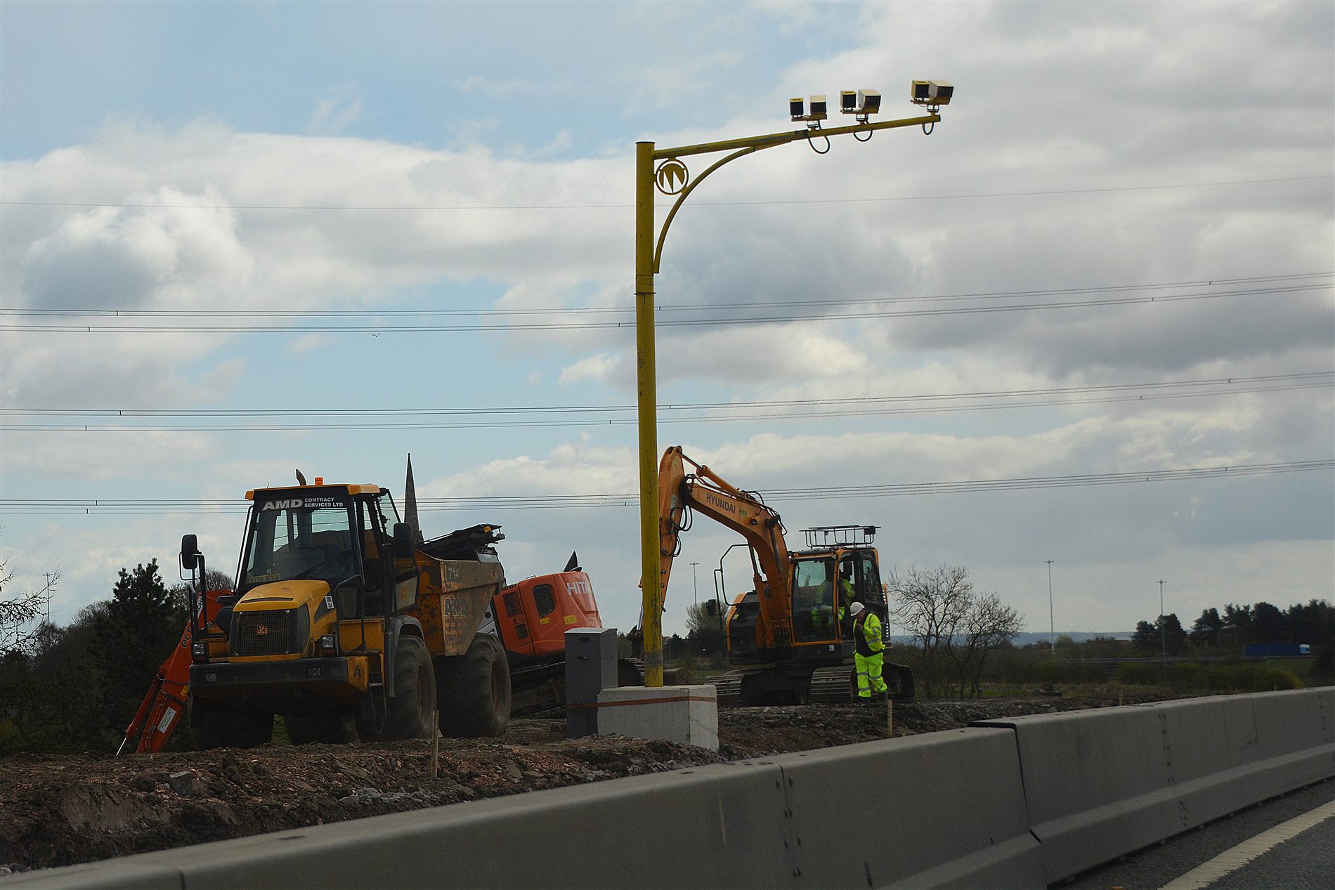 Motorway improvement works with excavators and dumpers alongside a concrete barrier